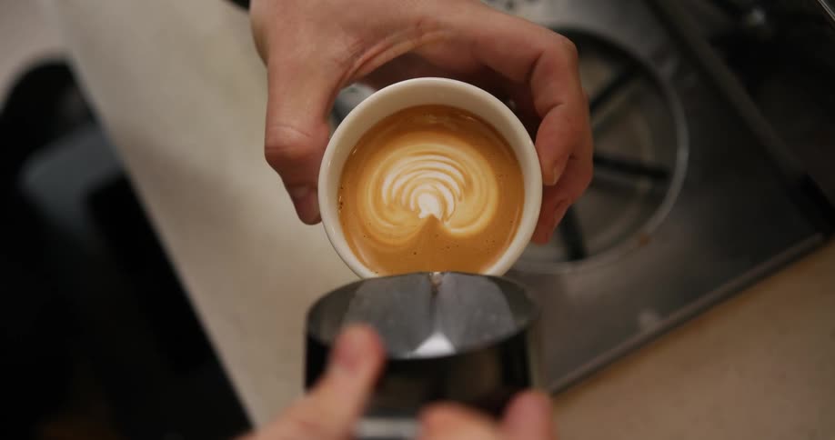 A man pours steamed milk into a latte