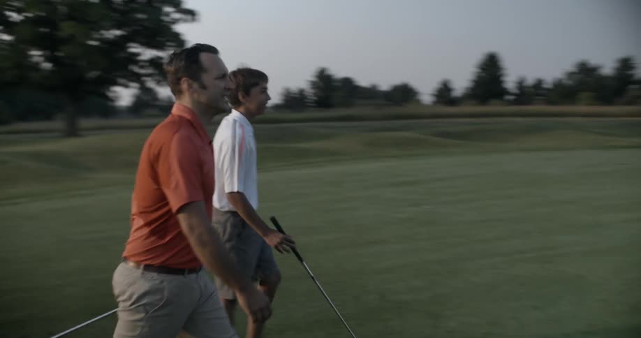 Two men walk on a golf course carrying golf clubs