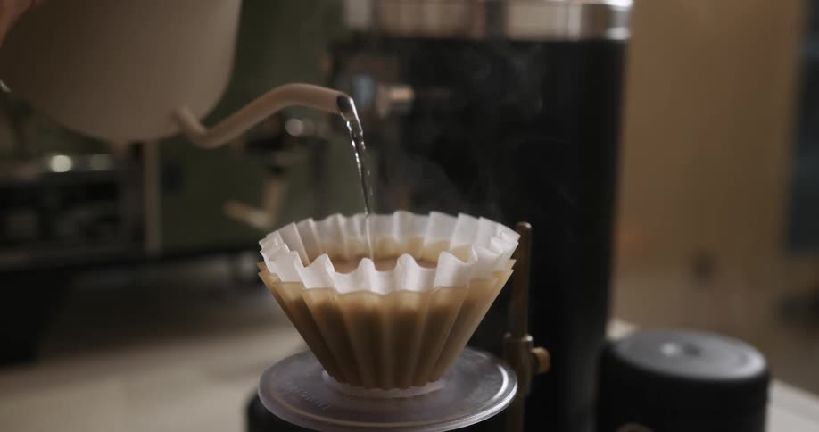 Person pours hot water over coffee grounds from pitcher to brew coffee