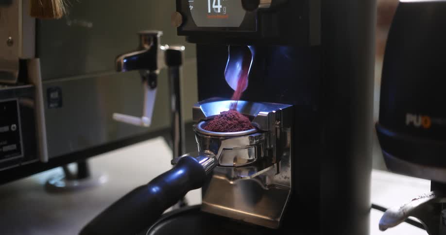 A modern coffee grinding machine is dispensing grinds into a small cup while displaying the current weight on a digital screen