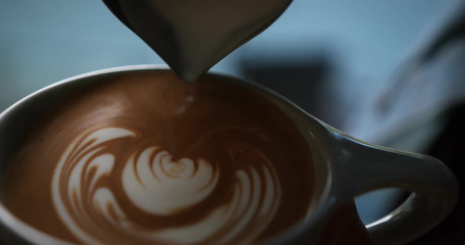 A person pours milk into a latte