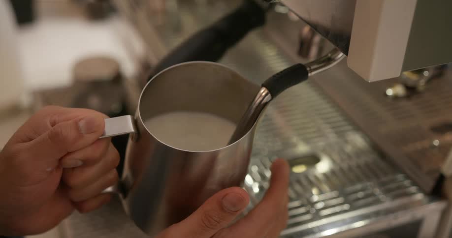 Person making coffee beverage holds milk as machine stirs it