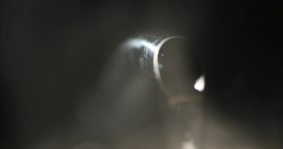 Steaming hot water pouring out of te spout of a teapot inside a dark room