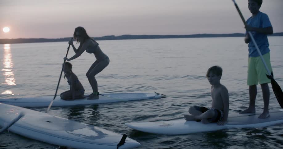 People are rowing on surf boards as one falls off into the water