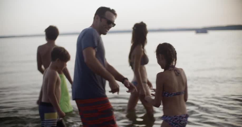 A man and woman wade in shallow water with their children in the evening