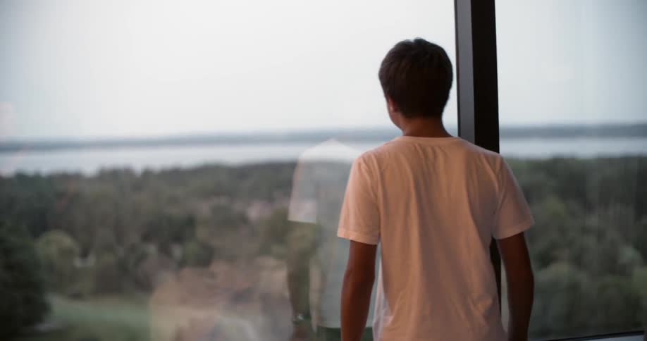 A boy walks over to look out of a window