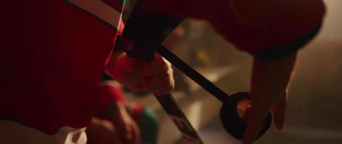 A kid is standing inside a room as sunlight shines in the window wrapping black tape around a hockey stick