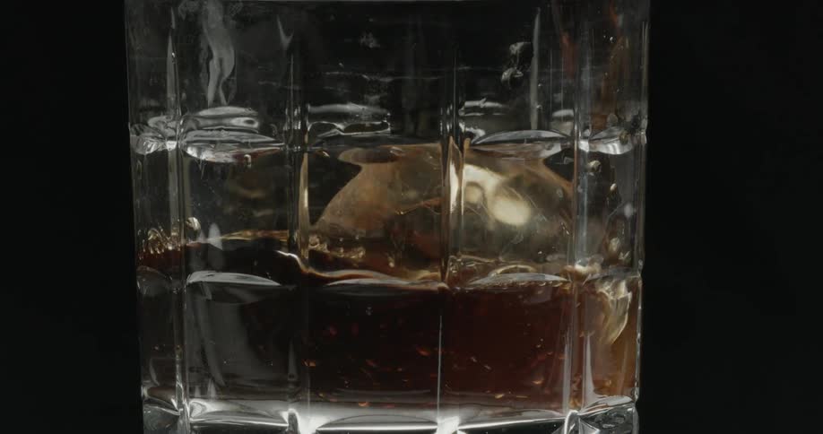 A beverage being poured over ice in a glass cup