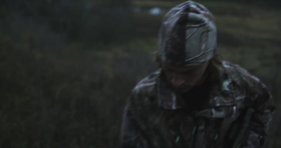 A hunter walks through a field with a crossbow