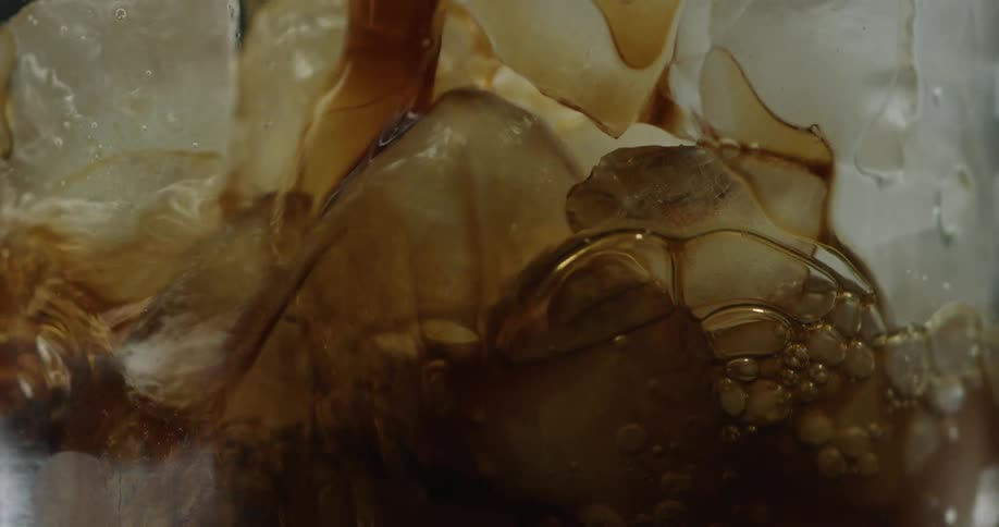 Close up of coffee pouring over ice cubes inside of a clear glass