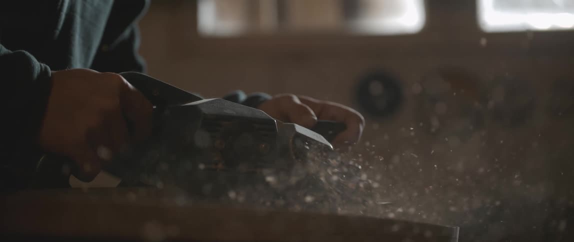 Sawdust fills the air in garage as person sands board with power tool