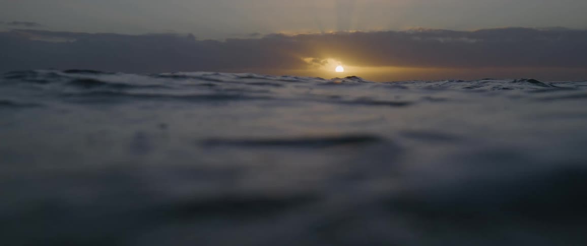 The sun setting over ocean waves on a cloudy evening