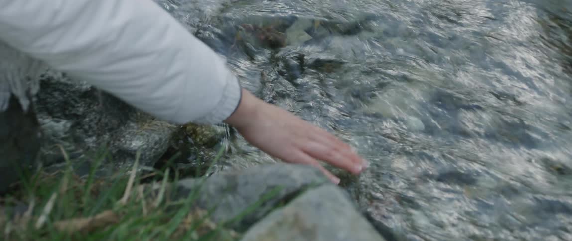 A woman leans down to put her hand in a stream
