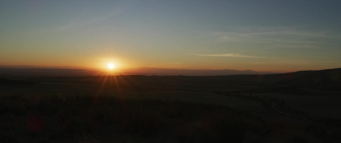 The sun setting over a grassland with hills in the far distance