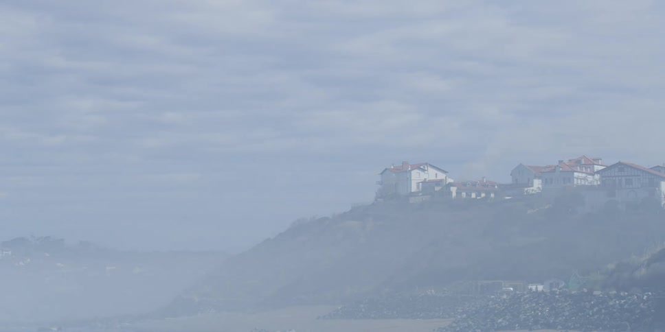 People move along slope leading to water as fog covers nearby town