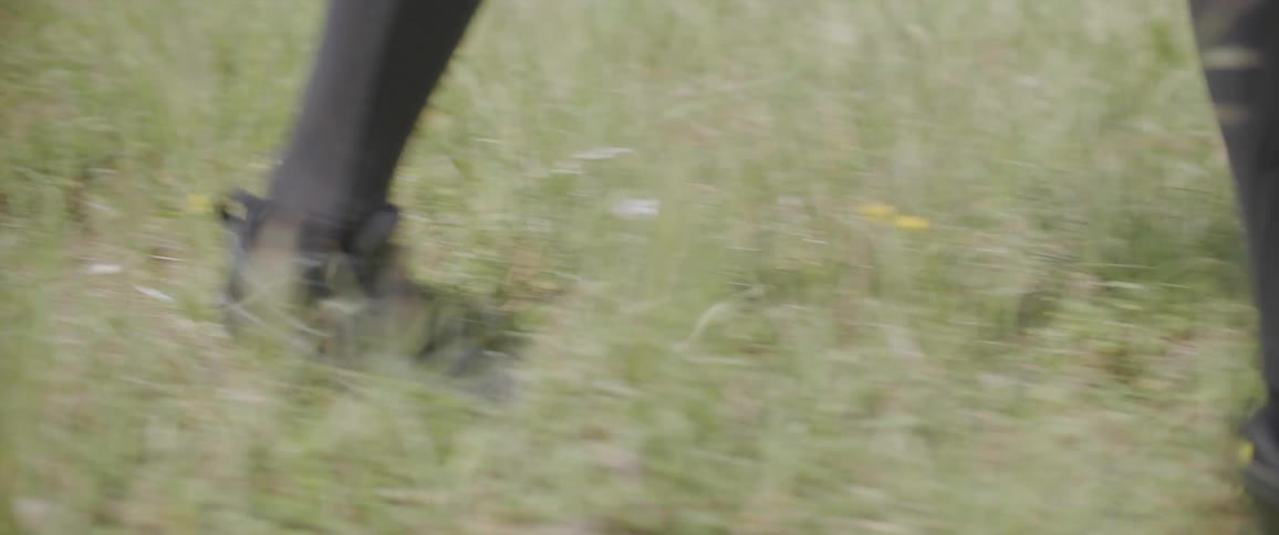 Close up of the feet of a person walking on a field of green grass
