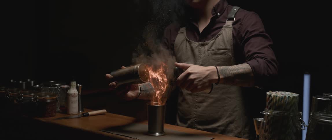 A bartender using a torch while preparing a beverage at a counter