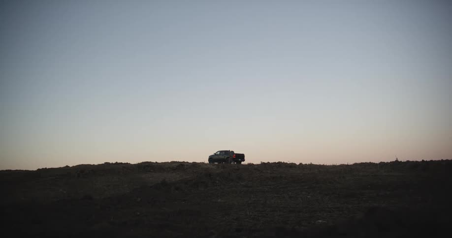 A person closing the back of a truck parked in a rural field