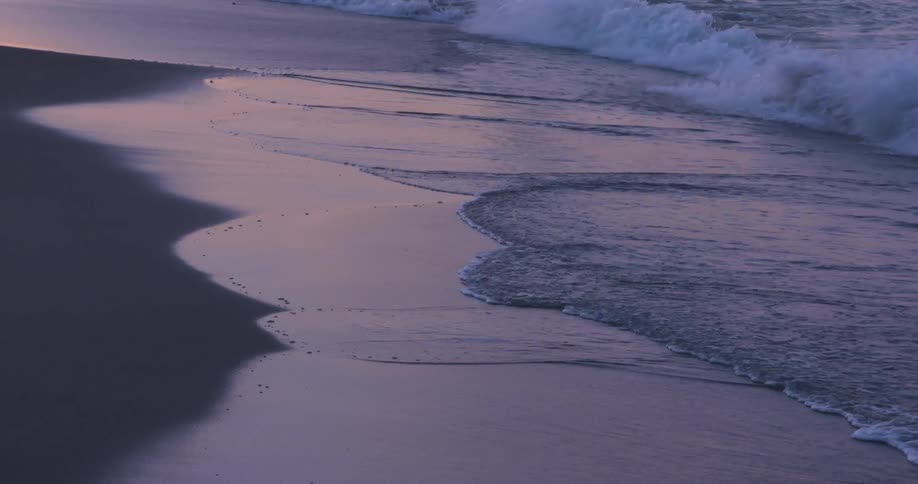 Gentle waves rolling over the wet sand on a beach at evening
