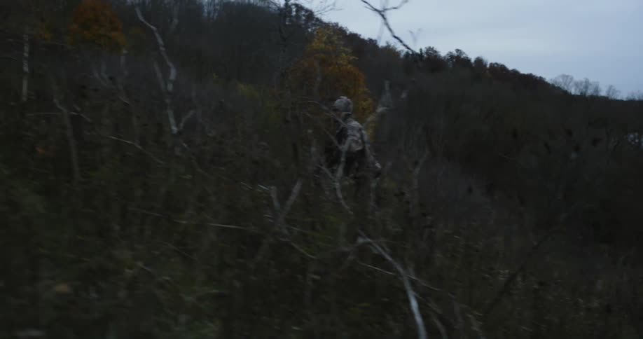 A hunter carries a crossbow up a hill