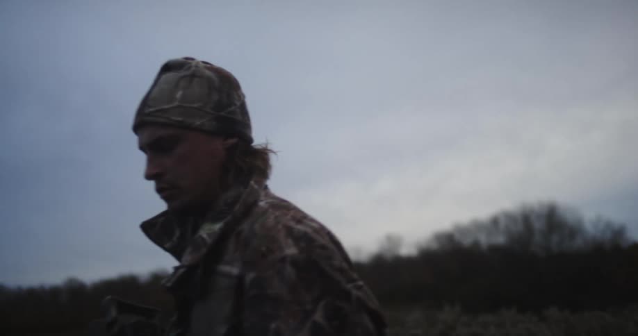 A man is standing outside holding a crossbow and looking through the scope