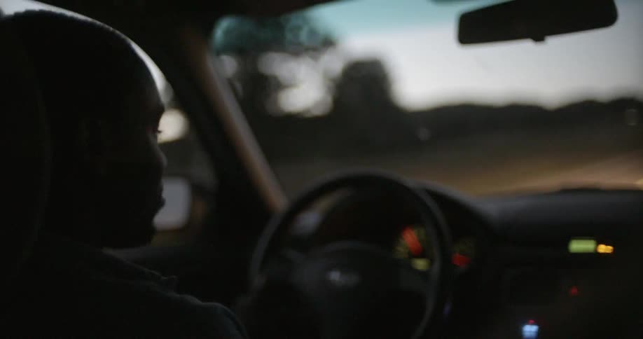 A man driving a car at dusk glances into the back seat