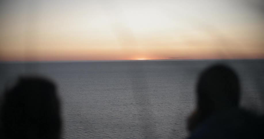 Two people sit near the ocean at dusk and talk