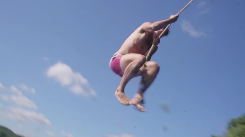 A man swings into a lake on a rope swing on a sunny day