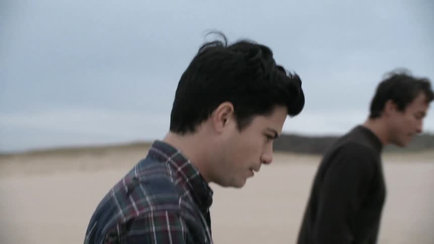 A couple and their older son walk on a beach on an overcast day
