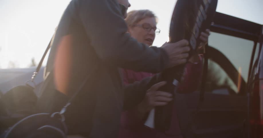 A man and woman unpack sports equipment from their vehicle