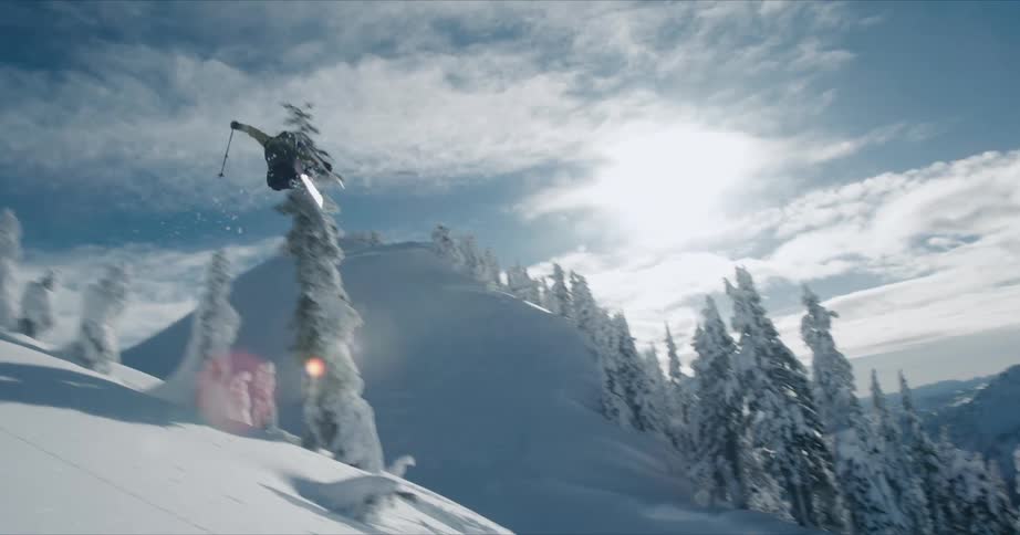 Skier takes jump of ramp and turns midair before skiing down slope on sunny day