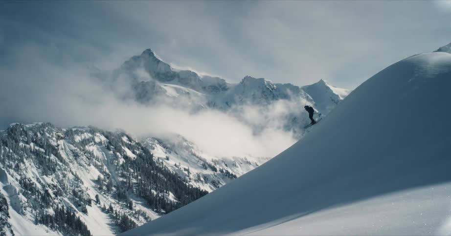 A skier is coasting down a snow covered mountain slope as they fly into the air and twist before landing back on the slope