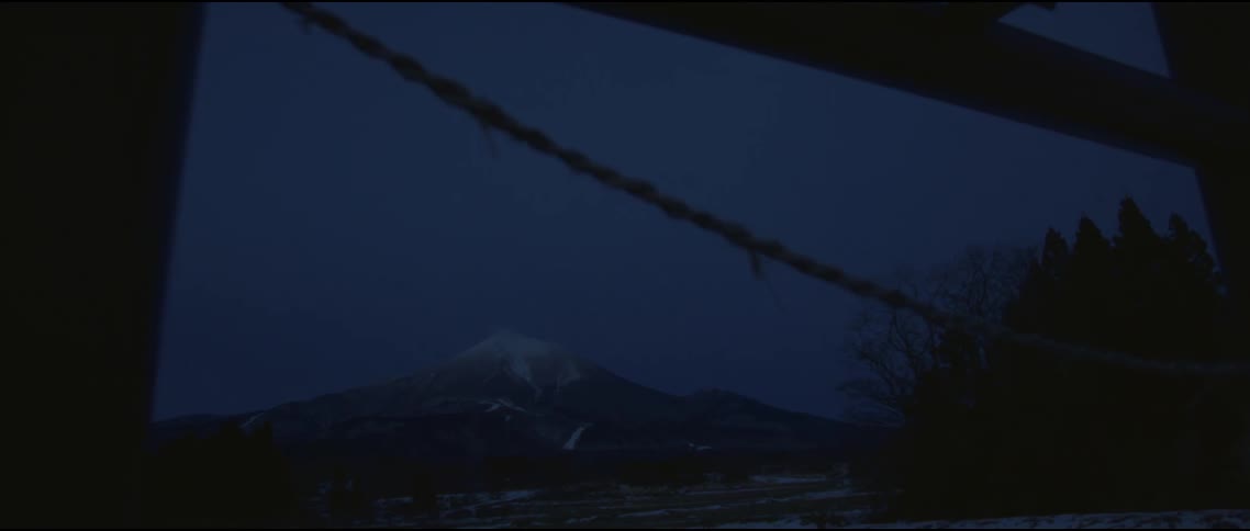 Silhouette of a fence with a rope swaying with trees and a snow covered mountain in the distance under a dark blue sky