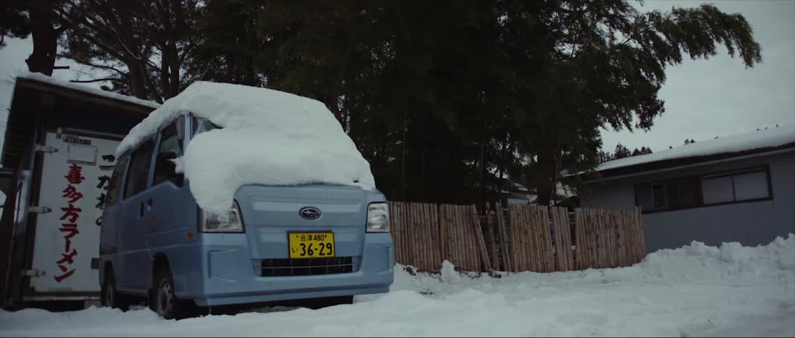 A van covered in a snow sits outside a house