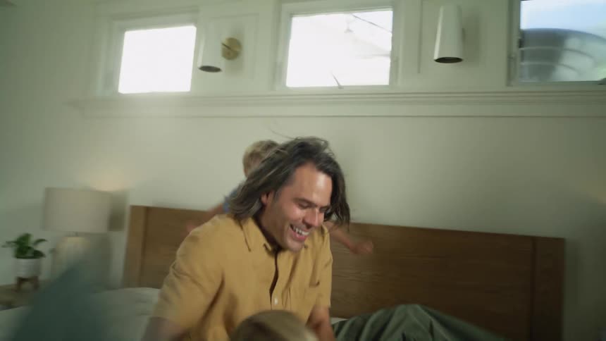 Father and sons have a pillow fight over the bed in the bedroom at home