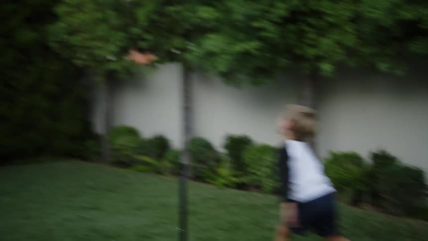 A man plays catch with his young son on a green grass side yard