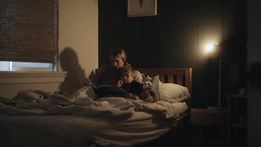 A woman sits in bed with her son and reads a book to him