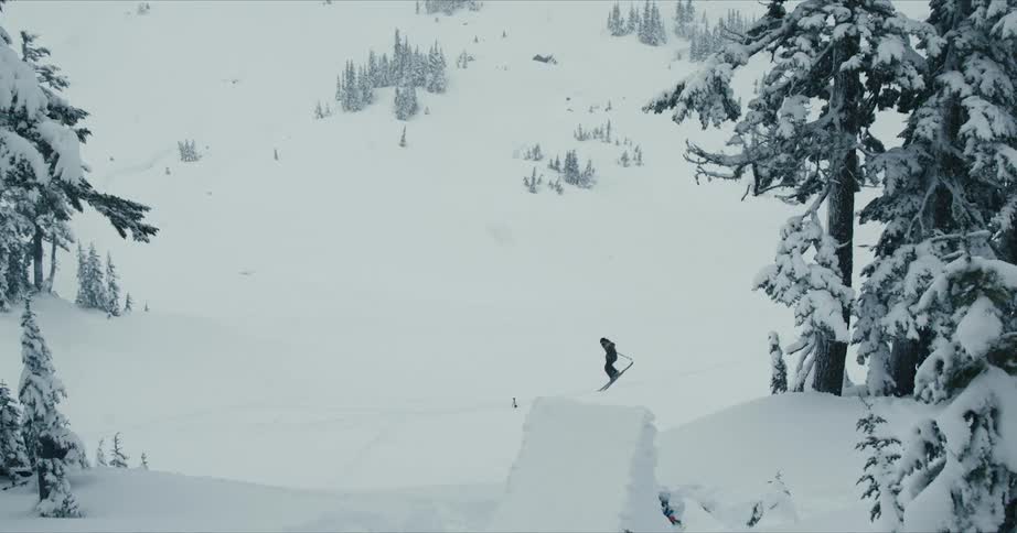 A skier skiing down a slope and off a jump doing a flip in the air