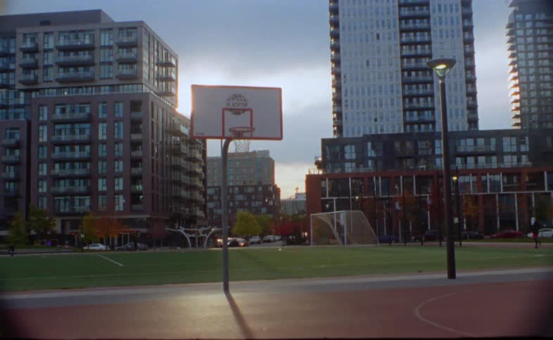 A basketball court is in a downtown park with tall buildings and skyscrapers in the distance