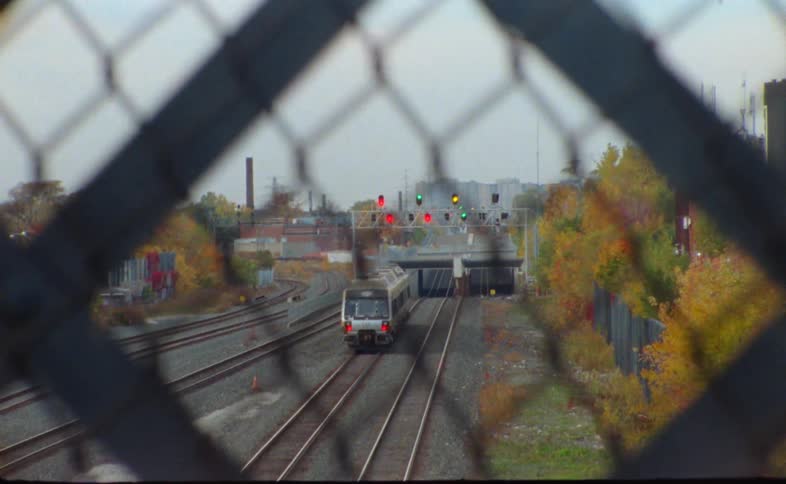 Chain link fence allows view of train traveling along train track toward town