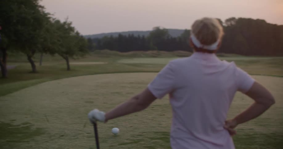 A man drives a golf ball as another watches