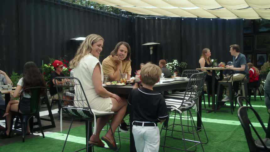 Parents watch son pretend to catch a baseball while they sit in temporary restaurant