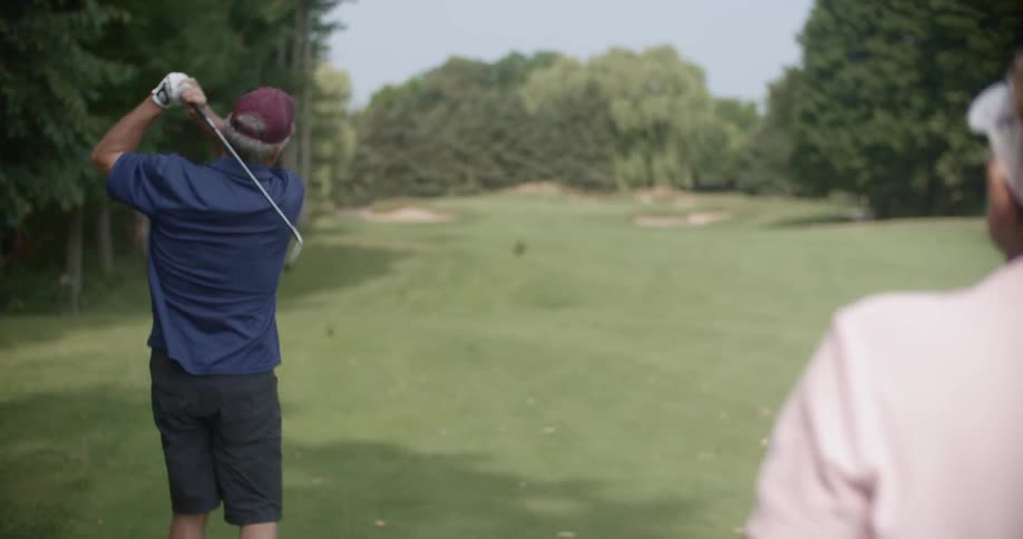 A man takes a swing at a golf ball on a golf course during the day