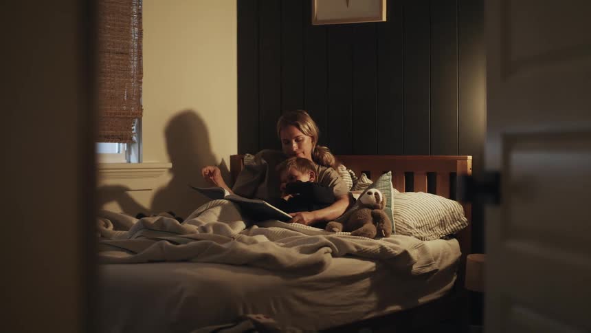 A mother and child read a book together while lying in bed