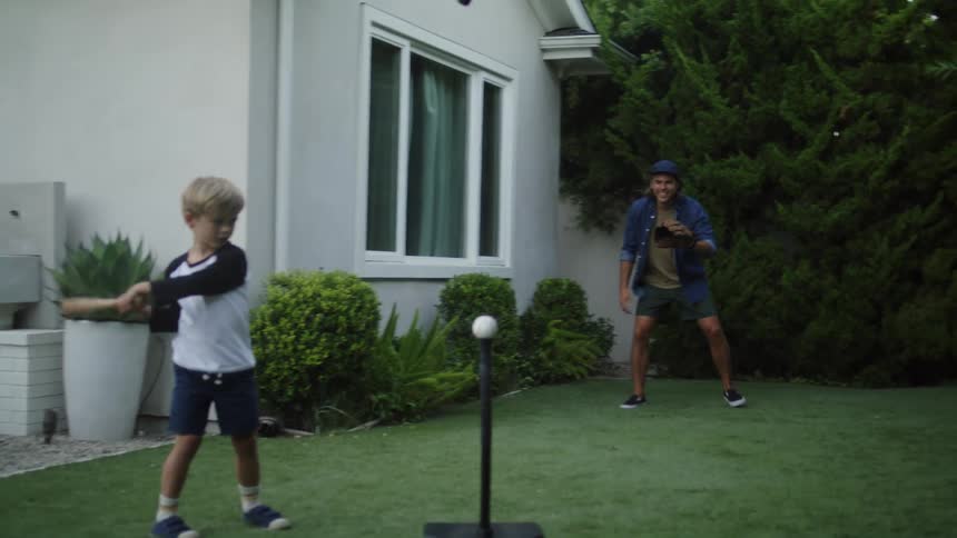 Father takes swing at baseball propped on holder and falls while father pursues ball
