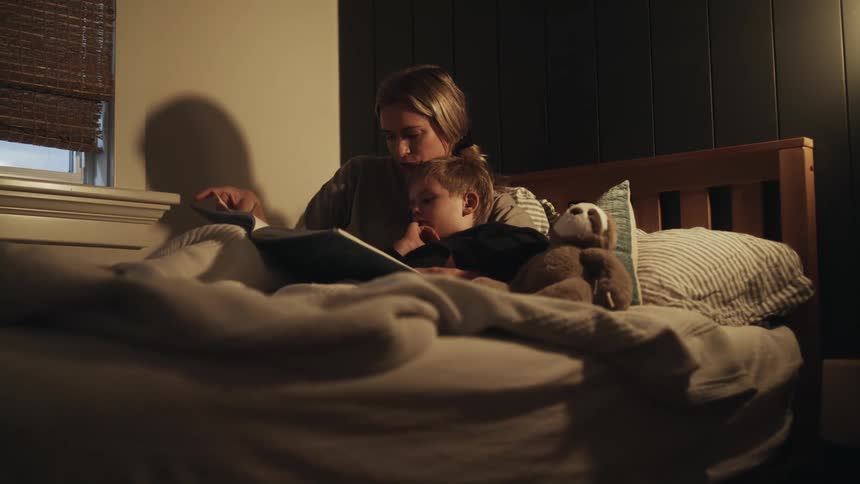 A mother reading to her toddler son in bed