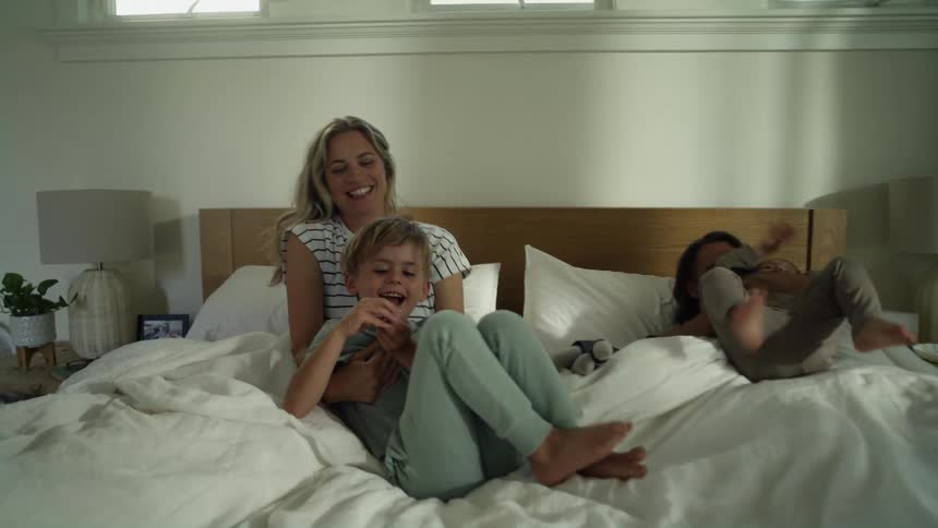 Parents play and cuddle with their children on bed