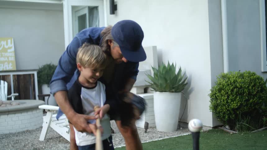 Father teaches son how to swing at ball in tball