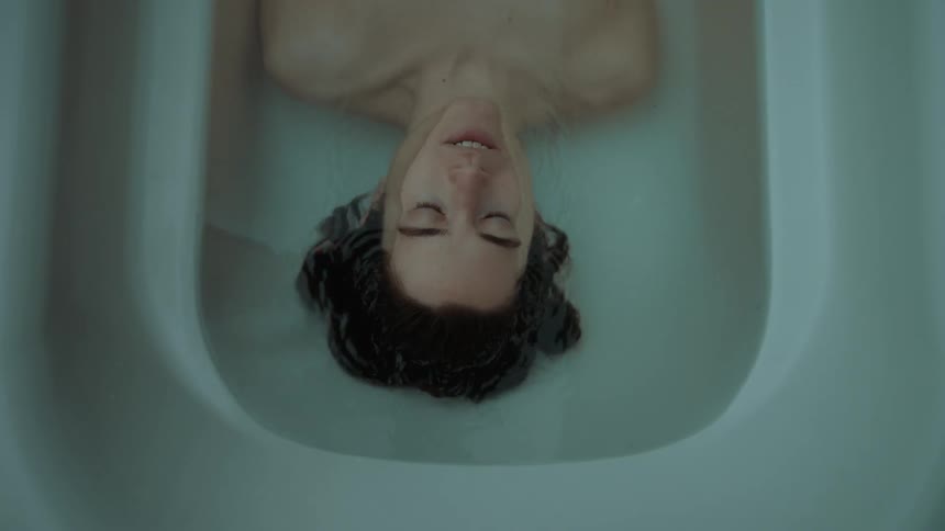 Woman floating in a white bathtub slowly submerges under water