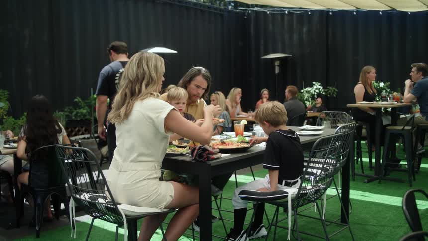 A man and a woman with their two small children are eating in a restaurant and a child is sitting on his fathers lap drinking orange juice